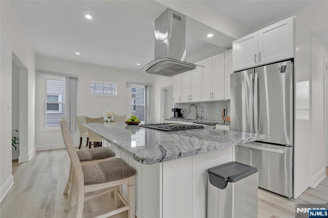 kitchen with light stone counters, island range hood, a kitchen island, white cabinets, and appliances with stainless steel finishes