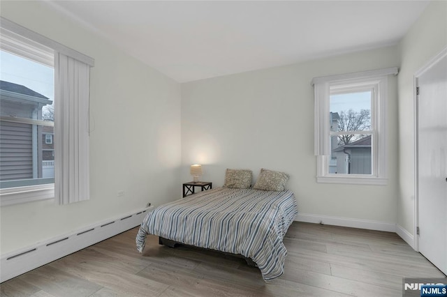 bedroom featuring baseboard heating, light wood-type flooring, and baseboards