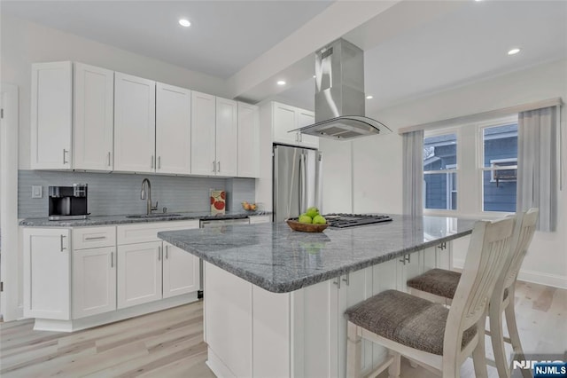 kitchen featuring island range hood, white cabinets, light stone counters, and freestanding refrigerator