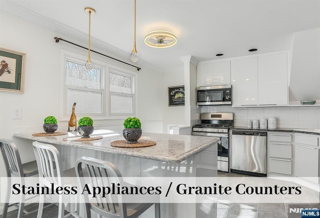 kitchen with decorative backsplash, appliances with stainless steel finishes, light stone countertops, crown molding, and white cabinetry