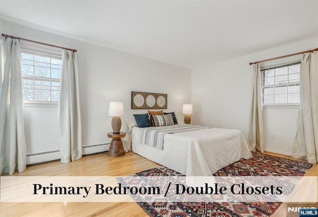 bedroom with multiple windows, baseboard heating, and wood finished floors