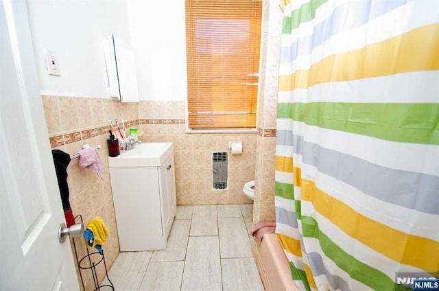 full bathroom featuring toilet, a wainscoted wall, tile walls, heating unit, and shower / bath combo with shower curtain