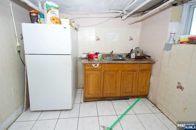 kitchen featuring brown cabinets, tile walls, freestanding refrigerator, light tile patterned flooring, and a sink