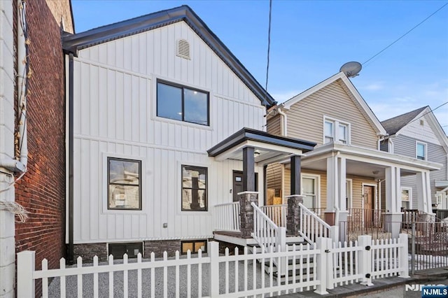 view of front facade featuring covered porch, a fenced front yard, and board and batten siding