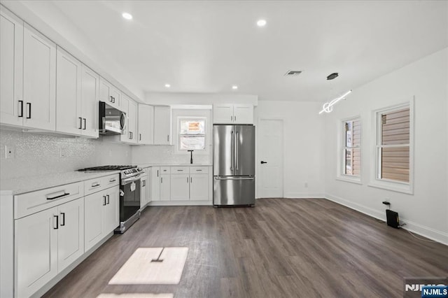 kitchen featuring stainless steel appliances, white cabinetry, dark wood finished floors, and decorative backsplash