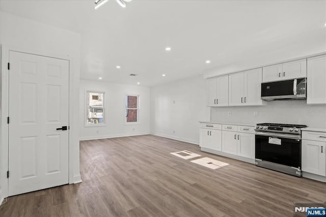 kitchen with light wood-style flooring, stainless steel appliances, white cabinets, open floor plan, and light countertops