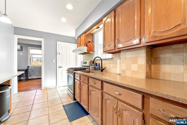 kitchen with under cabinet range hood, gas range, decorative backsplash, light tile patterned flooring, and a sink