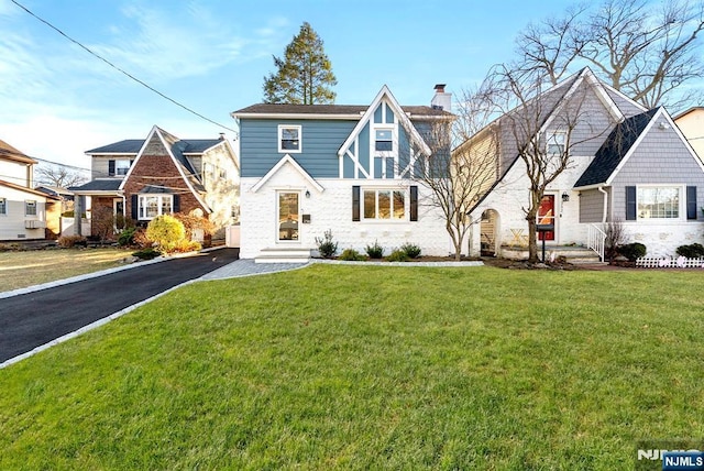 view of front of house with aphalt driveway, a chimney, and a front lawn