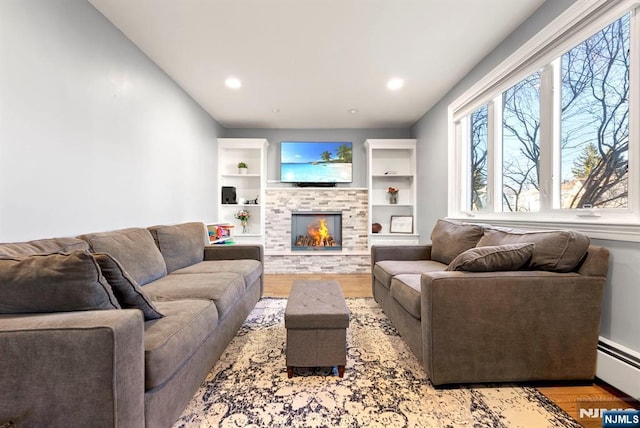 living room featuring recessed lighting, a warm lit fireplace, a baseboard heating unit, and wood finished floors