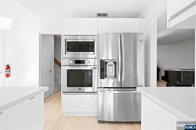 kitchen featuring stainless steel appliances, light countertops, visible vents, light wood-style floors, and white cabinets