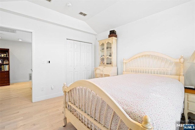 bedroom featuring light wood-style flooring, visible vents, baseboards, vaulted ceiling, and a closet