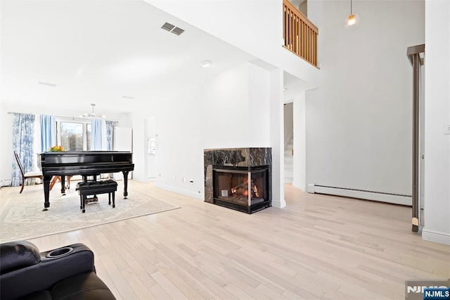 living room featuring a baseboard radiator, visible vents, light wood-style floors, a high end fireplace, and baseboards