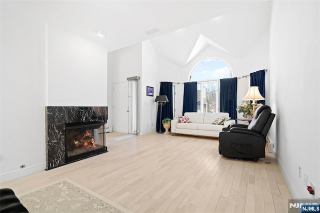 living room featuring high vaulted ceiling, a fireplace, wood finished floors, and visible vents