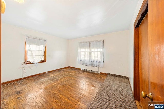 unfurnished room featuring radiator heating unit, baseboards, and wood finished floors