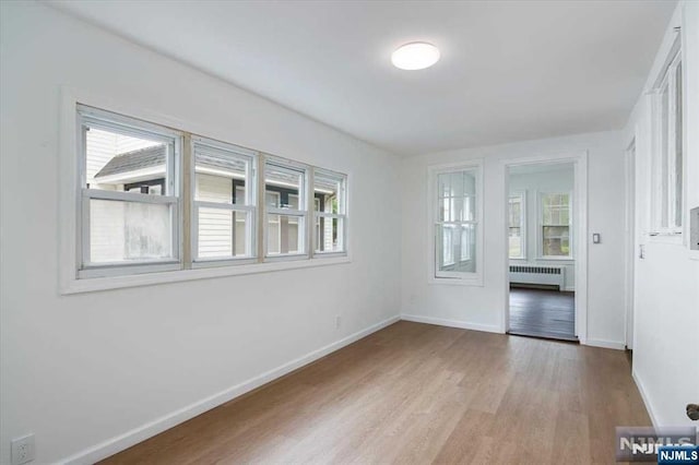 empty room with baseboards, light wood-type flooring, a wealth of natural light, and radiator