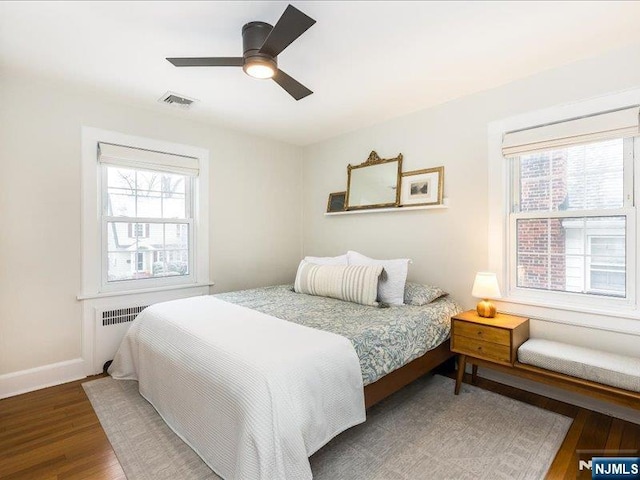 bedroom with dark wood-style flooring, multiple windows, visible vents, and baseboards