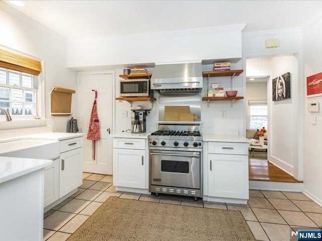 kitchen featuring wall chimney range hood, white cabinetry, stainless steel appliances, and light countertops