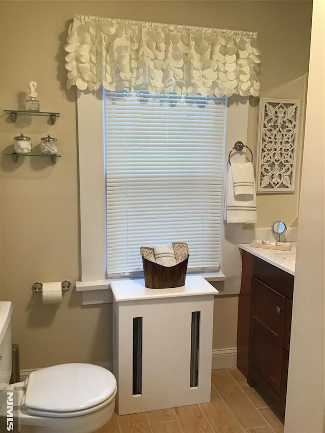 half bathroom with wood tiled floor, baseboards, vanity, and toilet