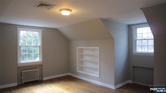 additional living space featuring built in features, visible vents, radiator heating unit, and wood finished floors