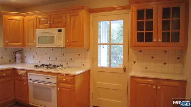 kitchen featuring white appliances, plenty of natural light, backsplash, and glass insert cabinets