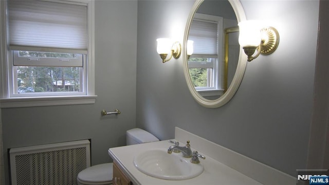 half bathroom with vanity, toilet, and radiator