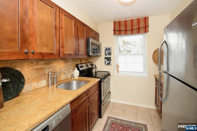 kitchen featuring a sink, light stone countertops, stainless steel appliances, backsplash, and light tile patterned flooring