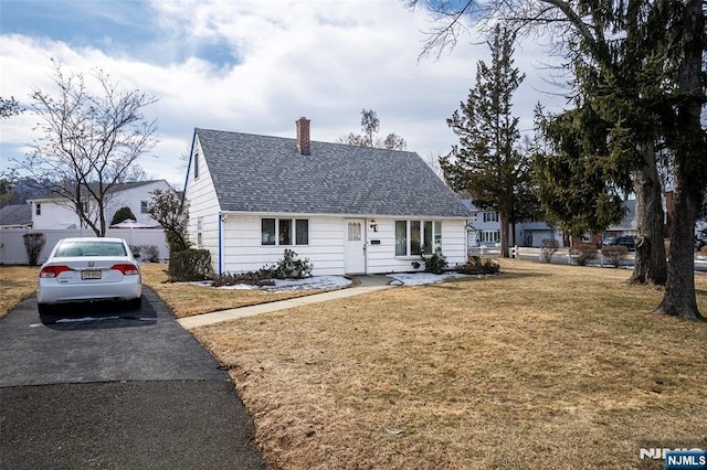 view of front facade with a shingled roof, a chimney, aphalt driveway, and a front yard