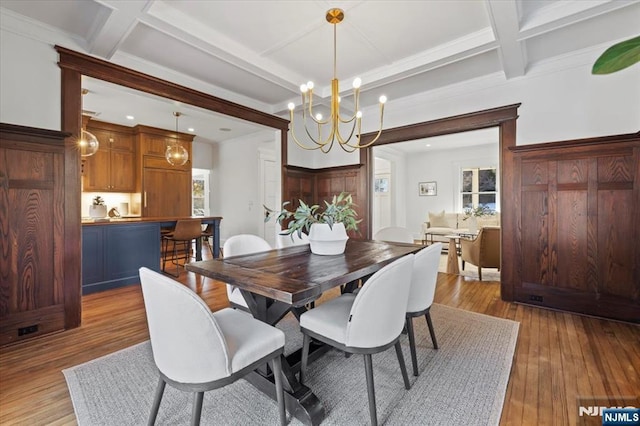 dining area with beam ceiling, coffered ceiling, light wood finished floors, and an inviting chandelier