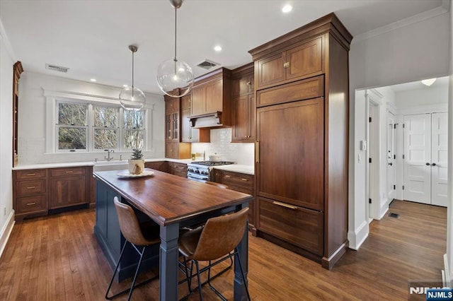 kitchen with visible vents, stainless steel range, a kitchen island, glass insert cabinets, and light countertops