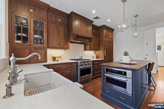 kitchen featuring stainless steel appliances, light countertops, visible vents, glass insert cabinets, and a sink