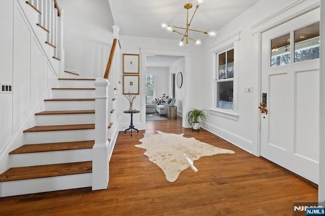 foyer entrance with an inviting chandelier, stairs, baseboards, and wood finished floors