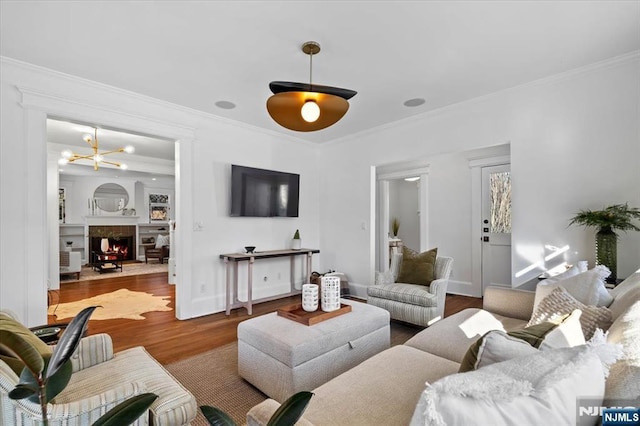 living area featuring a notable chandelier, a lit fireplace, wood finished floors, and crown molding