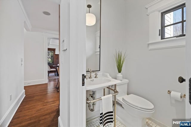 half bathroom with toilet, plenty of natural light, baseboards, and wood finished floors