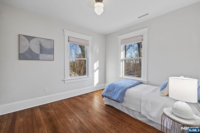 bedroom with multiple windows, wood finished floors, visible vents, and baseboards