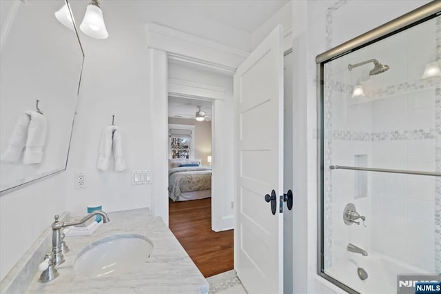 bathroom featuring ensuite bathroom, shower / bath combination with glass door, wood finished floors, vanity, and a ceiling fan