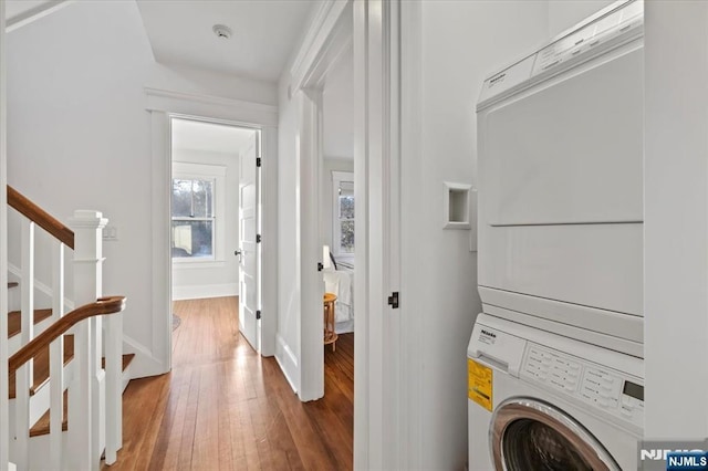 laundry area featuring stacked washer / dryer, laundry area, baseboards, and wood finished floors