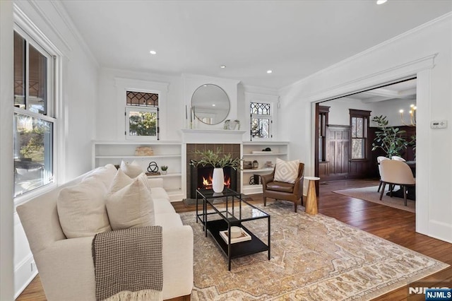 living room with a tile fireplace, recessed lighting, wood finished floors, baseboards, and ornamental molding