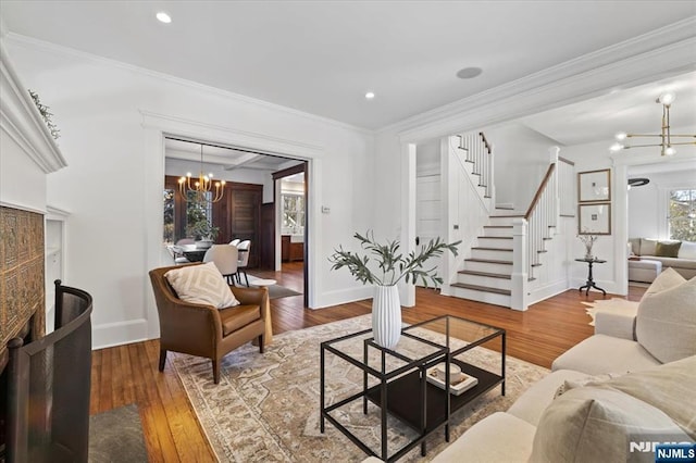 living area featuring a notable chandelier, wood finished floors, baseboards, stairway, and crown molding