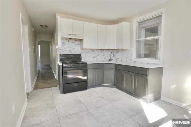 kitchen with tasteful backsplash, white cabinets, light countertops, black gas stove, and under cabinet range hood