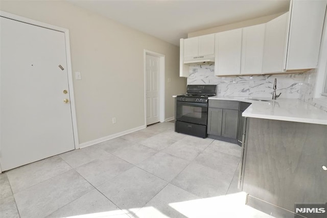 kitchen featuring black gas range, tasteful backsplash, light countertops, under cabinet range hood, and a sink