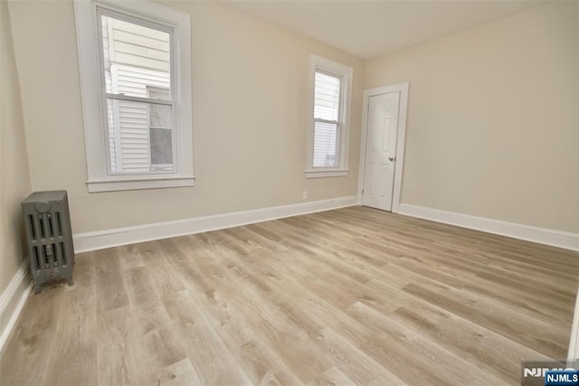 spare room featuring light wood-style floors, radiator heating unit, and baseboards