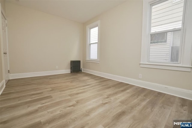 empty room with radiator heating unit, light wood-style flooring, and baseboards