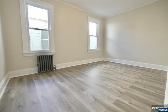 empty room with ornamental molding, radiator heating unit, wood finished floors, and baseboards