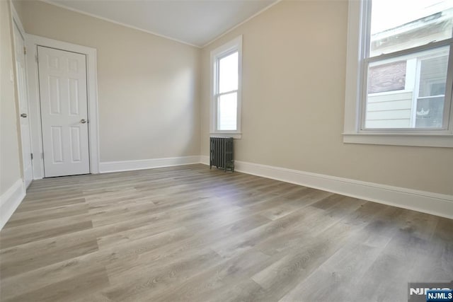 empty room featuring radiator, crown molding, baseboards, and wood finished floors