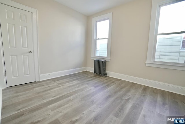 unfurnished room with radiator heating unit, wood finished floors, and baseboards