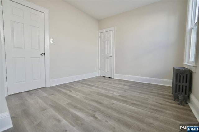 unfurnished room featuring baseboards, wood finished floors, and radiator