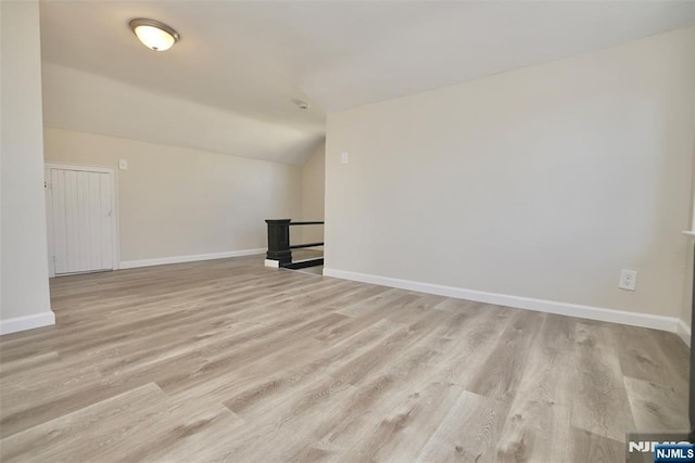 empty room featuring lofted ceiling, light wood-type flooring, and baseboards