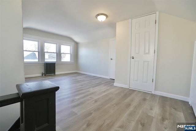 interior space featuring light wood finished floors, radiator heating unit, baseboards, and vaulted ceiling