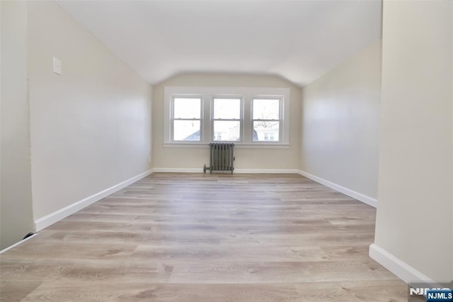 spare room featuring radiator heating unit, baseboards, vaulted ceiling, and wood finished floors