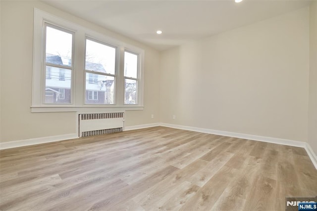 empty room with light wood finished floors, radiator heating unit, baseboards, and recessed lighting